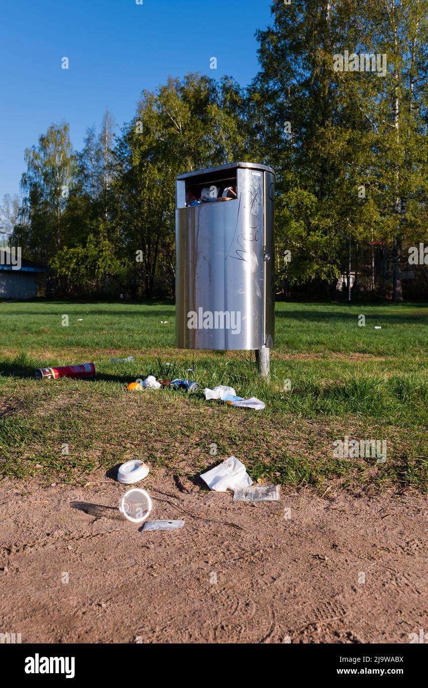 La spazzatura piena può con la spazzatura sul terreno intorno ad esso su una zona erbosa in estate Foto Stock