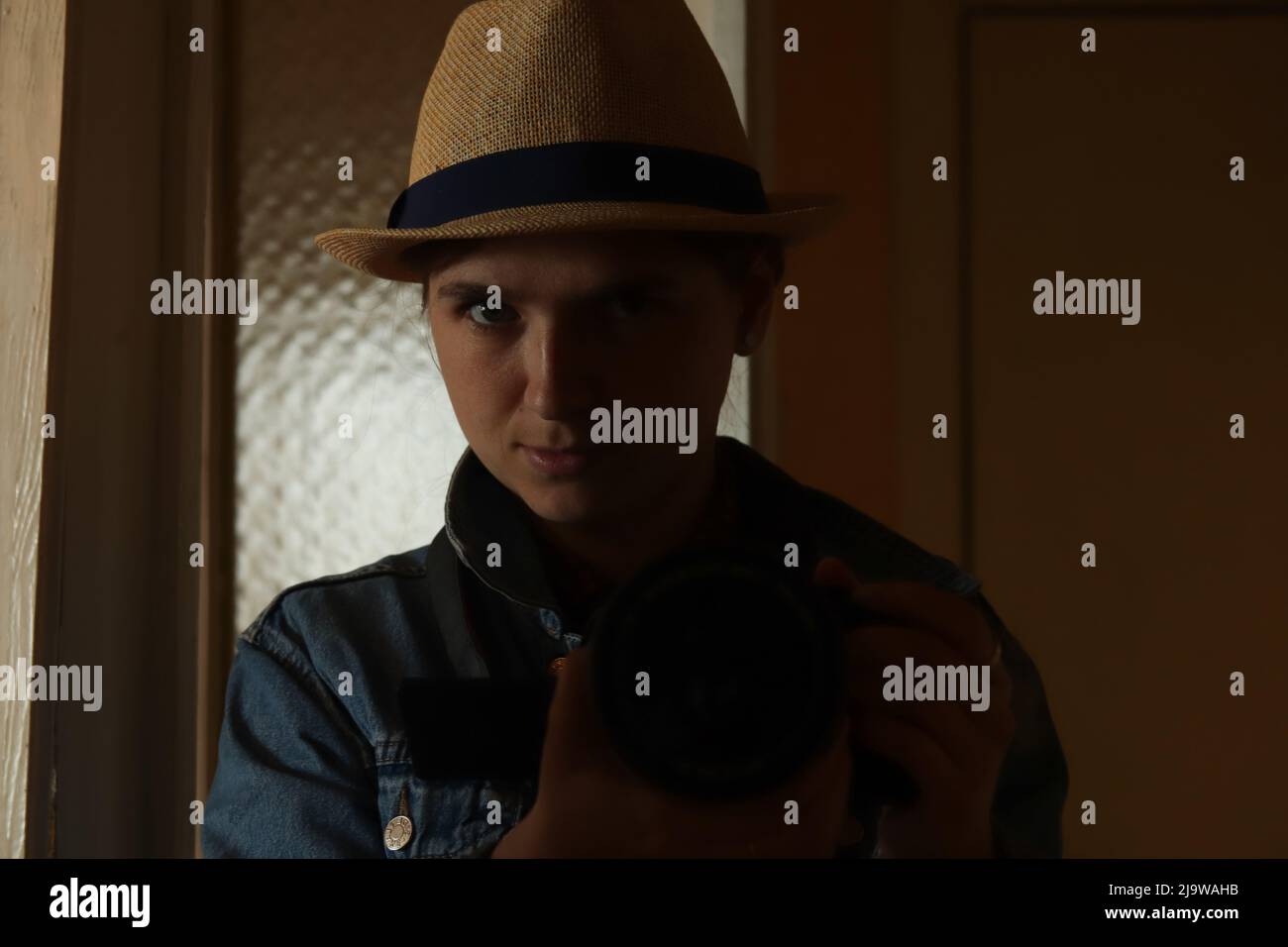 Defocus giovane donna prendere la fotografia in riflessione specchio. Donna millenaria in cappello. Ritratto nero scuro. Salute mentale. Narcisismo. Fotografia seria Foto Stock