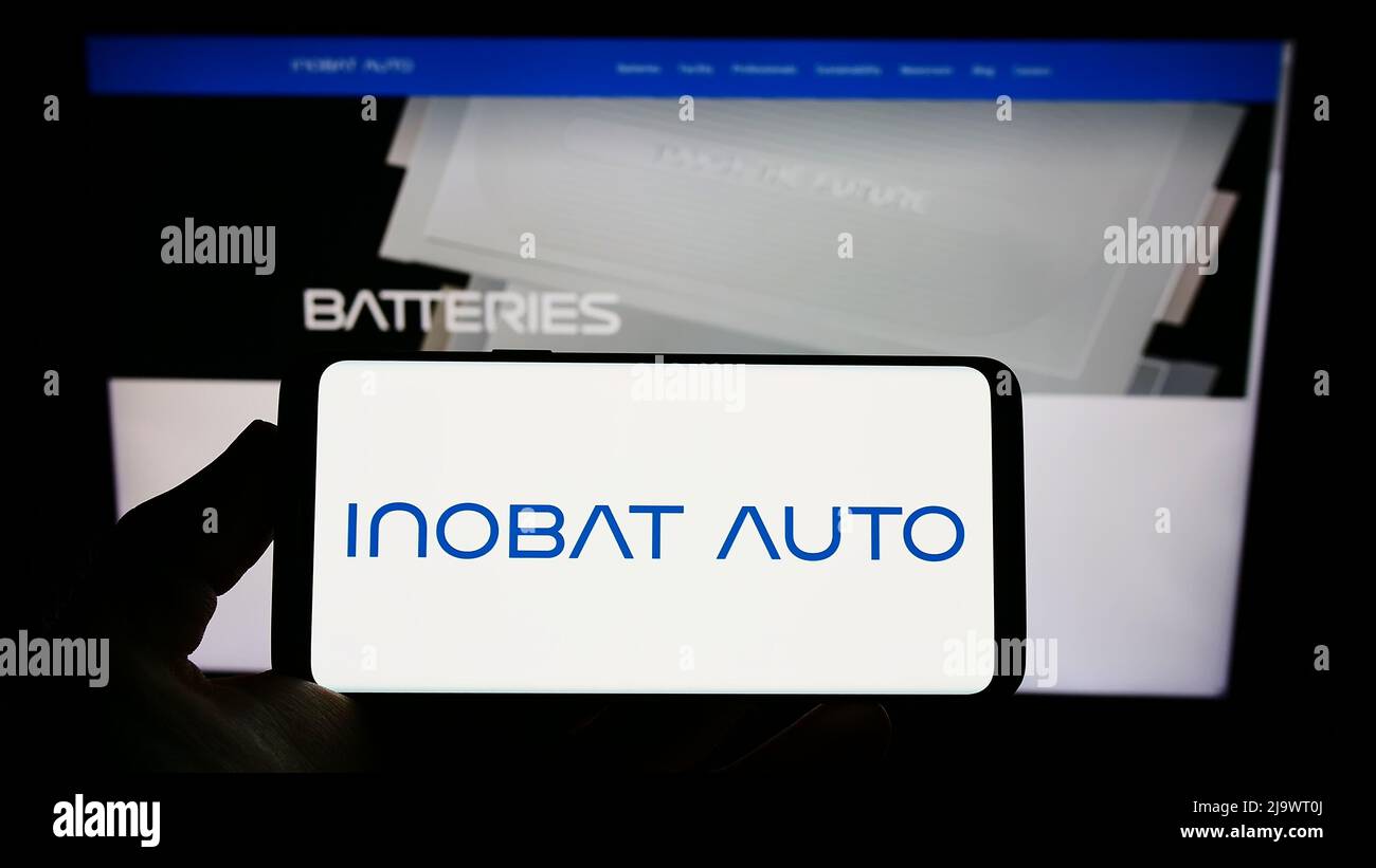 Persona che tiene il telefono cellulare con il logo della società slovacca di batterie InoBat Auto sullo schermo di fronte alla pagina web aziendale. Mettere a fuoco sul display del telefono. Foto Stock