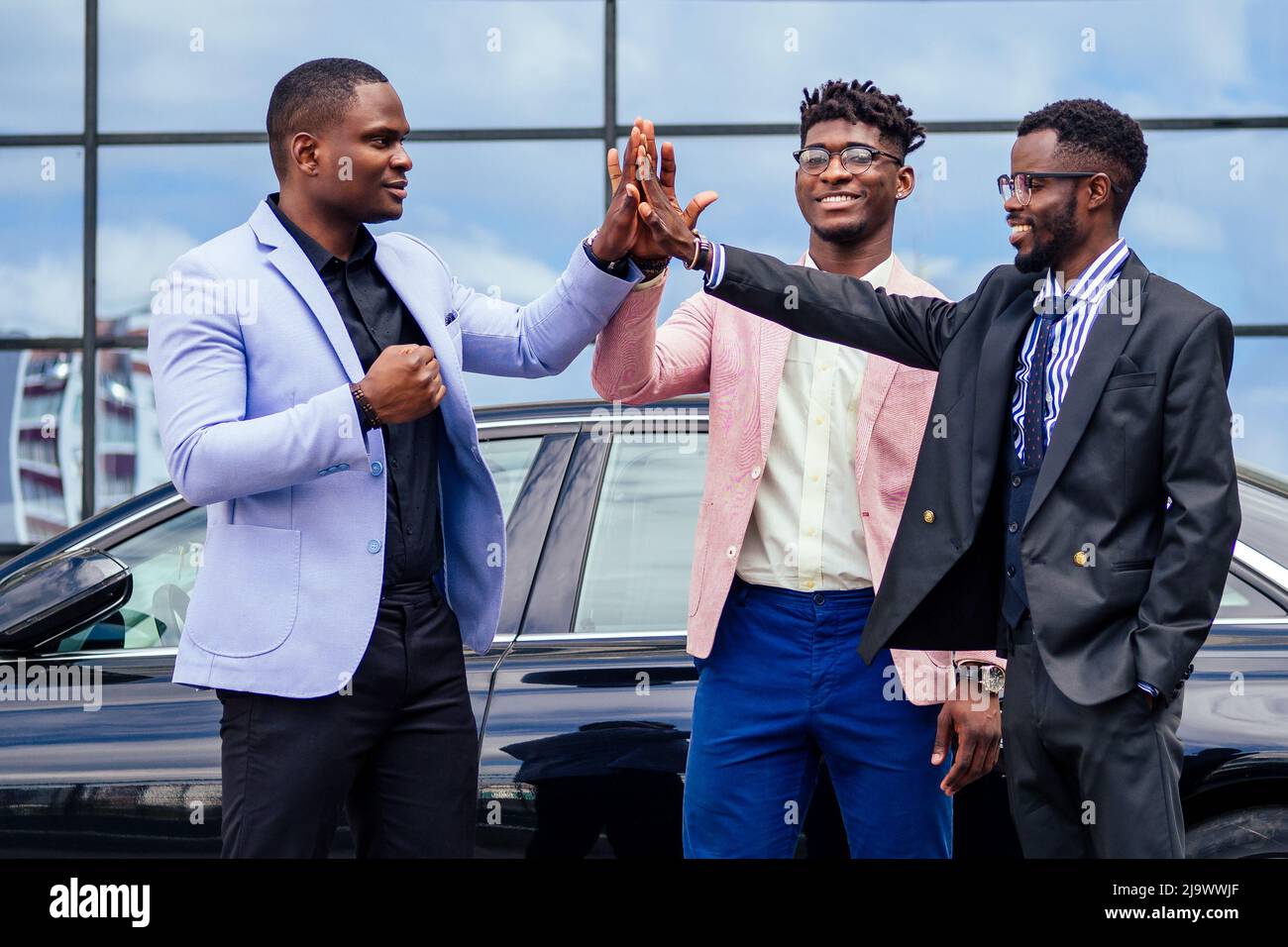 Un gruppo dei loro tre uomini d'affari africani americani di successo in un abito elegante che parla e gioisce sulla strada grattacielo finestra sfondo Foto Stock