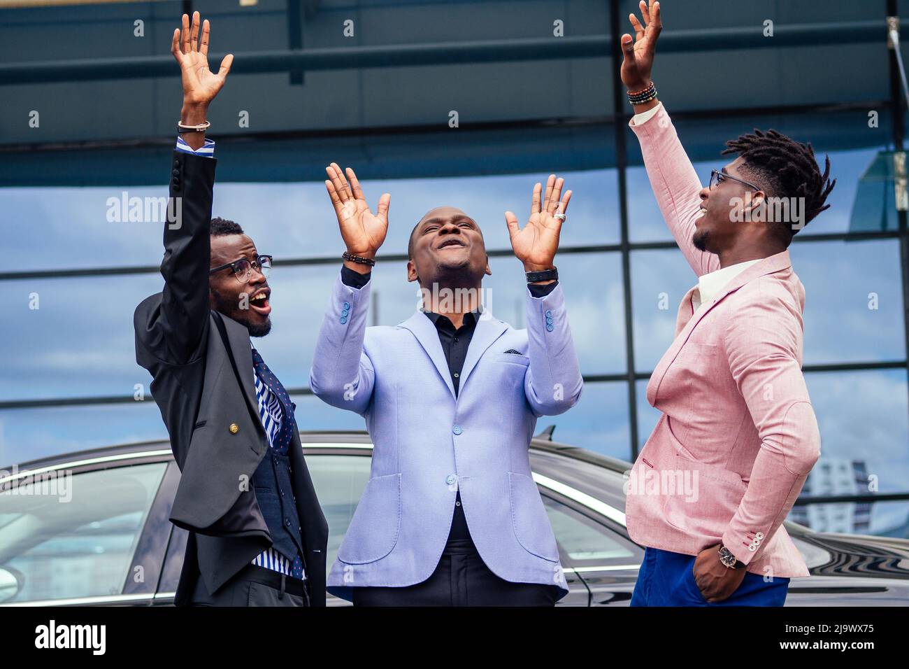 Un gruppo dei loro tre uomini d'affari africani americani di successo in un abito elegante che parla e gioisce sulla strada grattacielo finestra sfondo Foto Stock