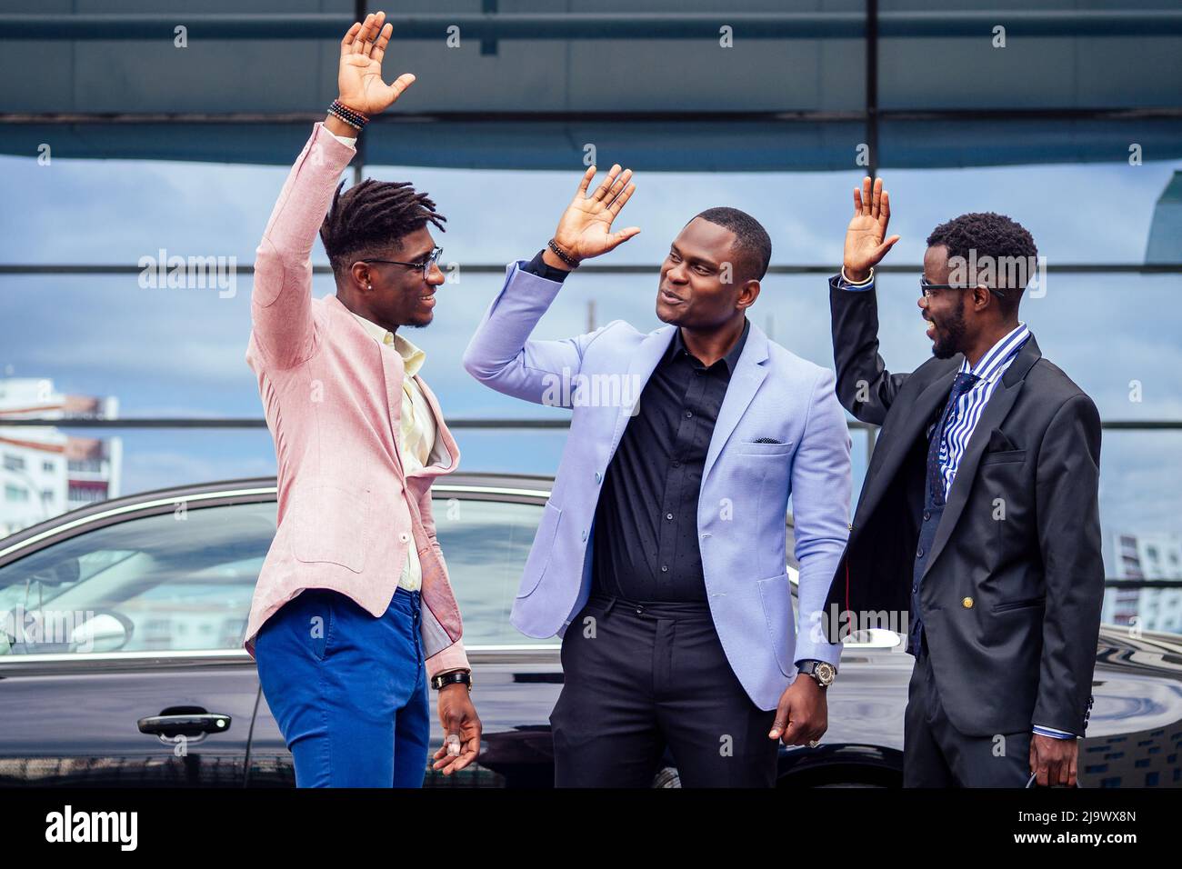 Un gruppo dei loro tre uomini d'affari africani americani di successo in un abito elegante che parla e gioisce sulla strada grattacielo finestra sfondo Foto Stock