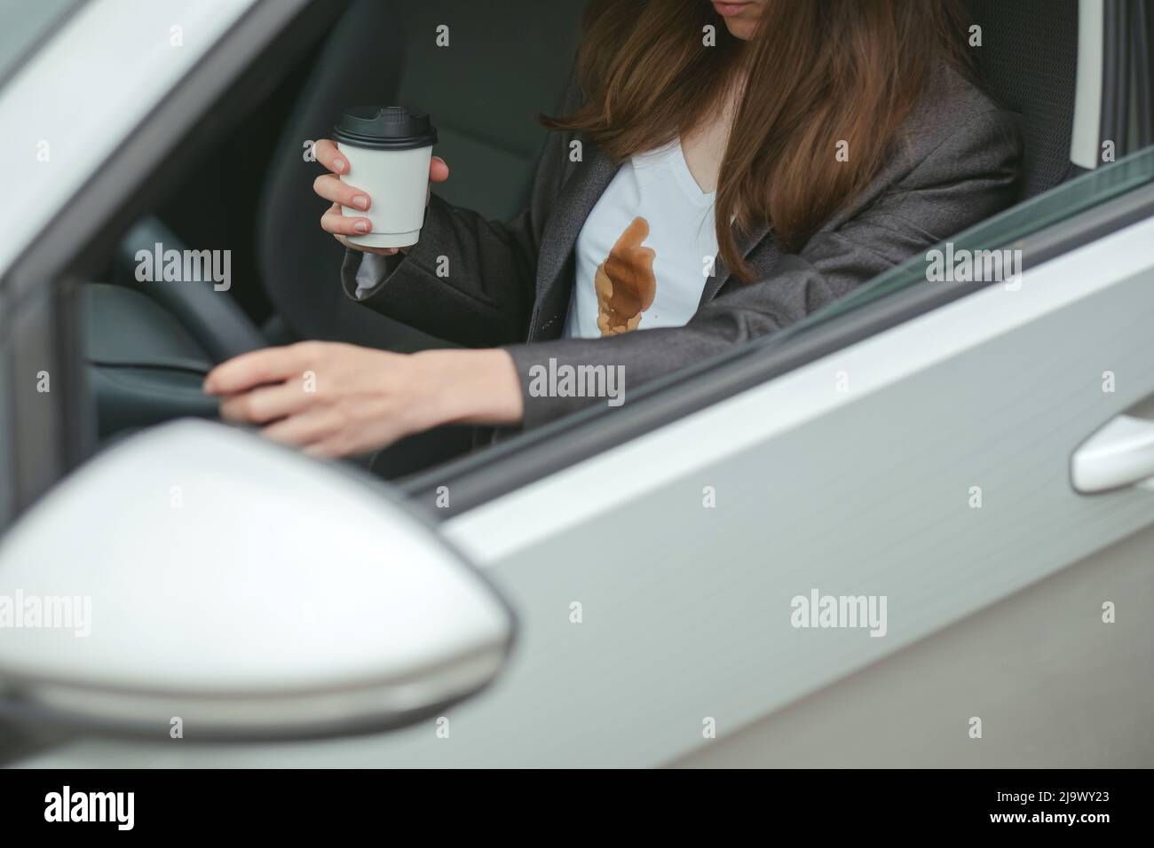 La donna di affari ha versato il caffè sulla camicia dietro il volante di un'automobile. Concetto di pulizia delle macchie sui vestiti Foto Stock