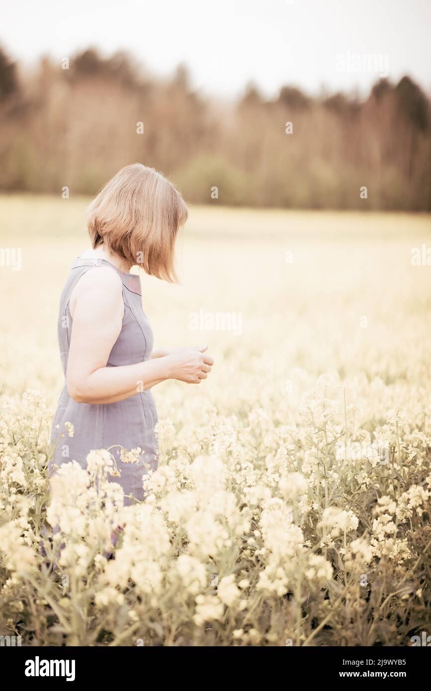 Concetto Mindfulness; salute delle donne; Una donna caucasica di mezza età in piedi in un campo di fiori in primavera, in profilo, immagine chiave alta, Suffolk UK Foto Stock
