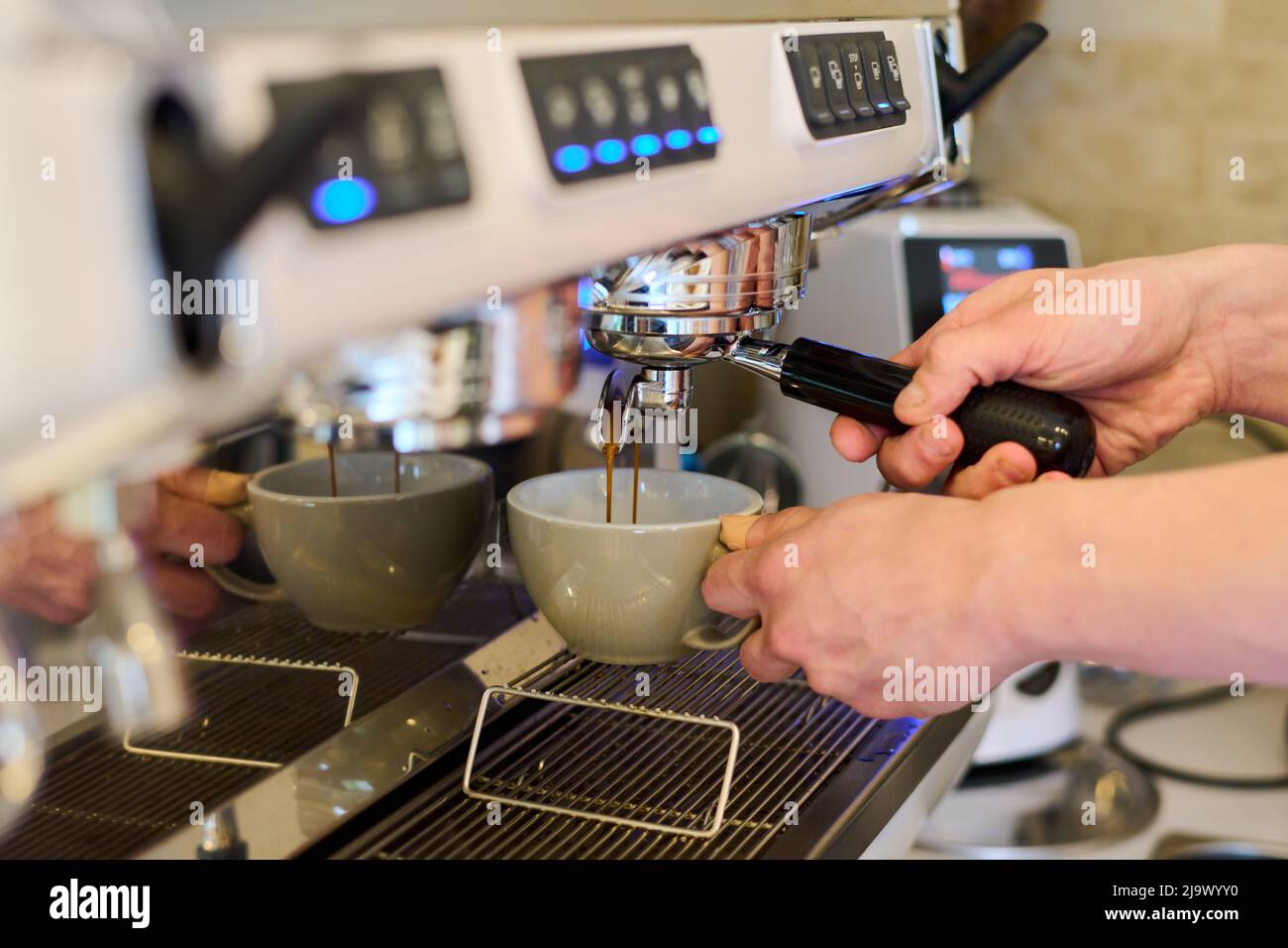 Primo piano di un barista professionista che tiene la tazza e prepara il caffè in una macchina da caffè carruba in un caffè Foto Stock