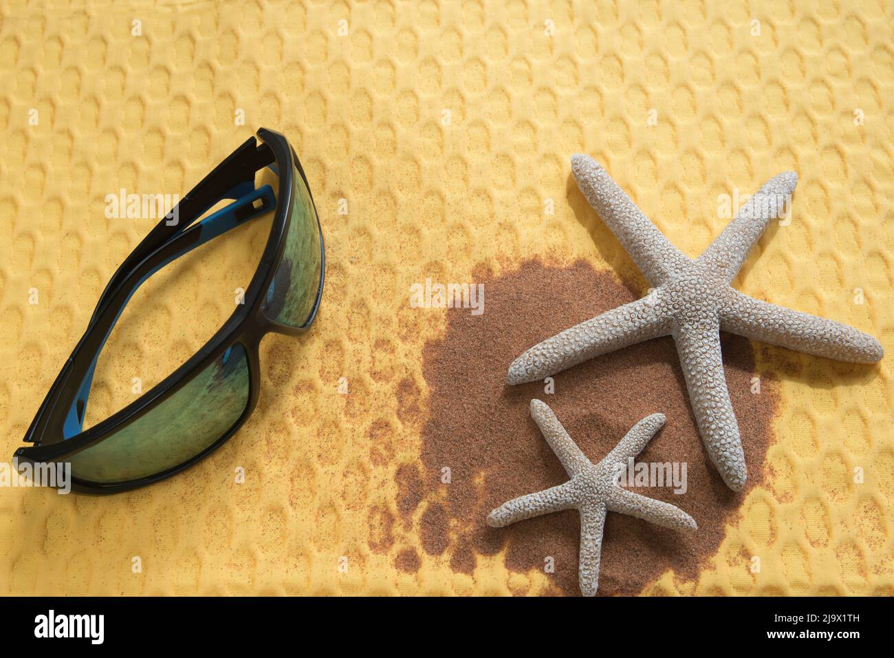 Concetto estivo, piatto con occhiali da sole, stelle marine e sabbia da spiaggia su un vibrante sfondo giallo Foto Stock