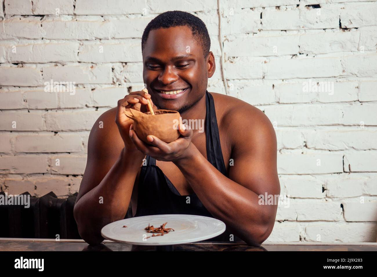 giovane e fiducioso uomo afroamericano in un grembiule nero scolpisce un vasaio da un laboratorio di ceramica di argilla. vaso di argilla in mano dell'artista latino Foto Stock