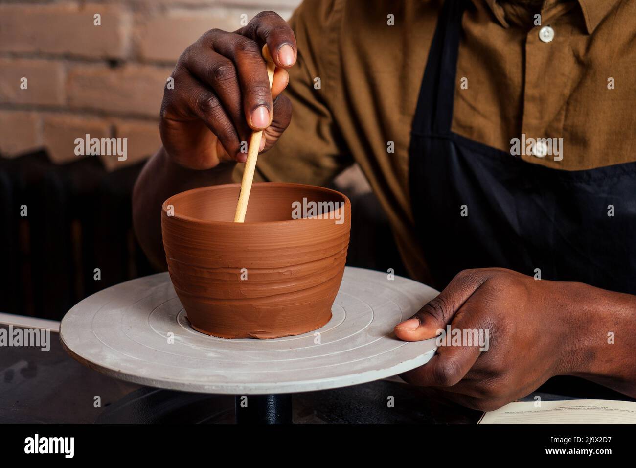 giovane e fiducioso uomo afroamericano in un grembiule nero scolpisce un vasaio da un laboratorio di ceramica di argilla. vaso di argilla in mano dell'artista latino Foto Stock