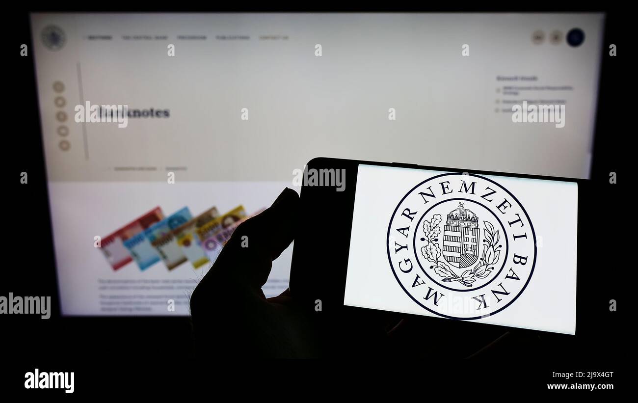 Persona che detiene il cellulare con il logo della Banca Nazionale Ungherese (Magyar Nemzeti Bank, MNB) sullo schermo di fronte alla pagina web. Mettere a fuoco sul display del telefono. Foto Stock