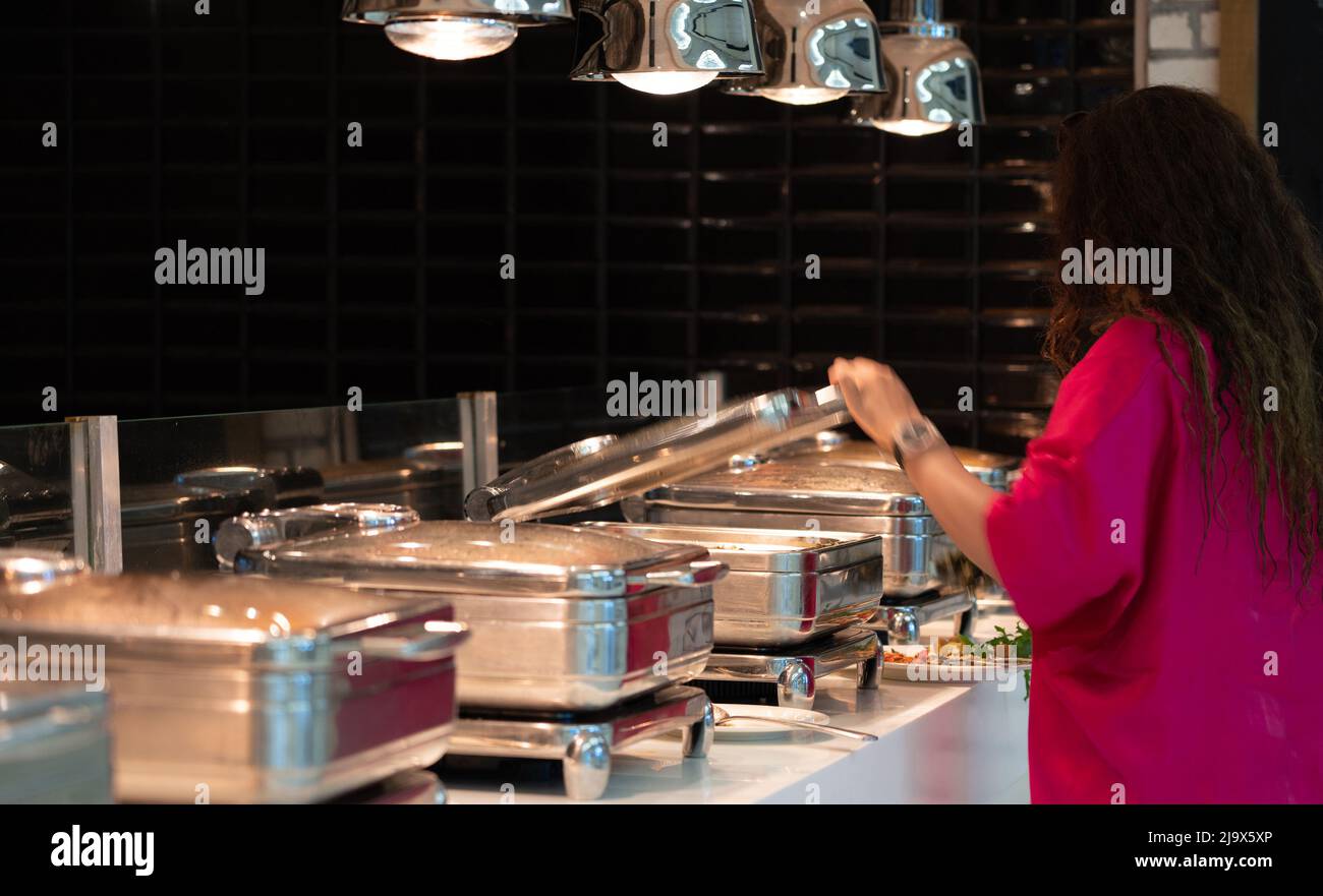 Donna che prende il cibo dai vassoi riscaldati nel buffet all-inclusive nel ristorante dell'hotel Foto Stock