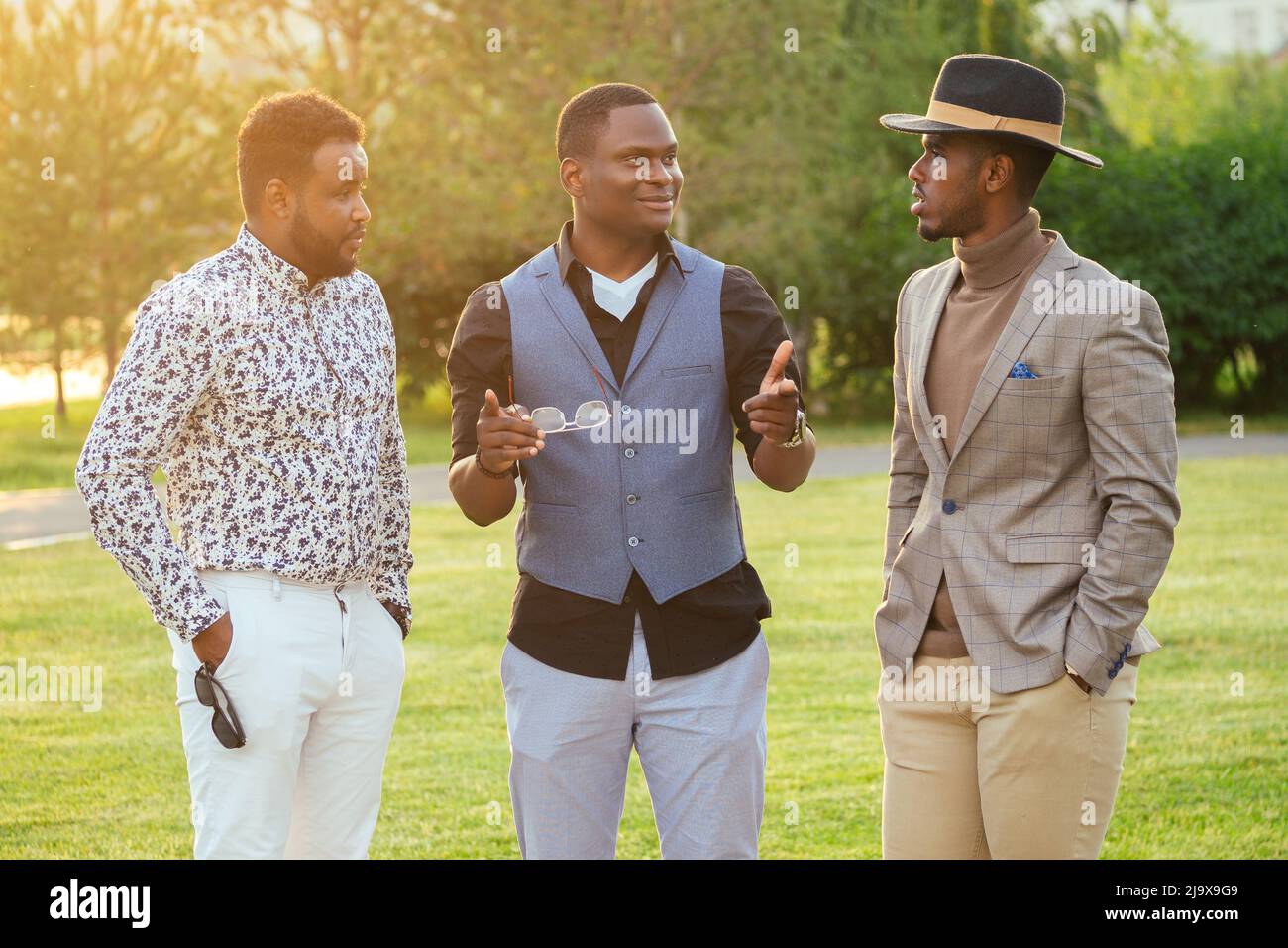 un gruppo di tre uomini neri in abiti eleganti in un parco estivo. Amici afroamericani ispanici businessman comunicante all'aperto Foto Stock