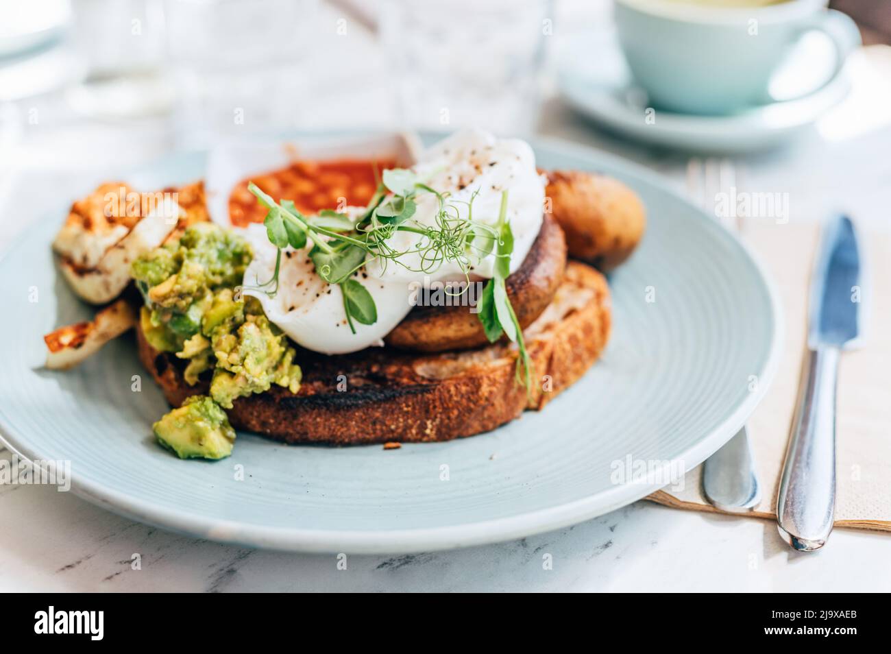 Colazione sana a base di uova in camicia, halloumi alla griglia, harissa tofu affumicato strapazzate, avocado schiacciato, funghi alla griglia e fagioli di pomodoro sul pane tostato Foto Stock