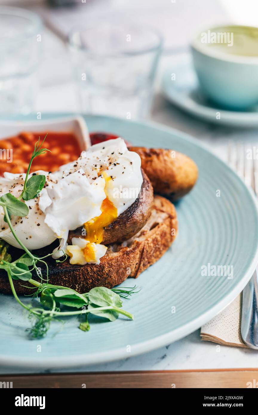 Colazione sana a base di uova in camicia, halloumi alla griglia, harissa tofu affumicato strapazzate, avocado schiacciato, funghi alla griglia e fagioli di pomodoro sul pane tostato Foto Stock