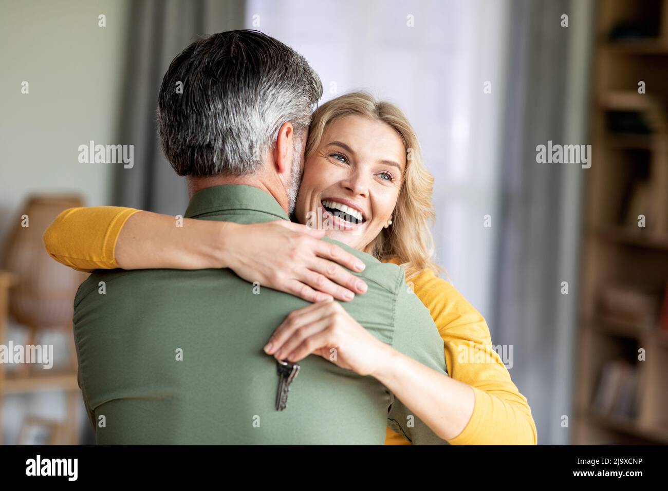 Donna felice di mezza età che abbraccia il marito e tiene le chiavi di casa in mano Foto Stock