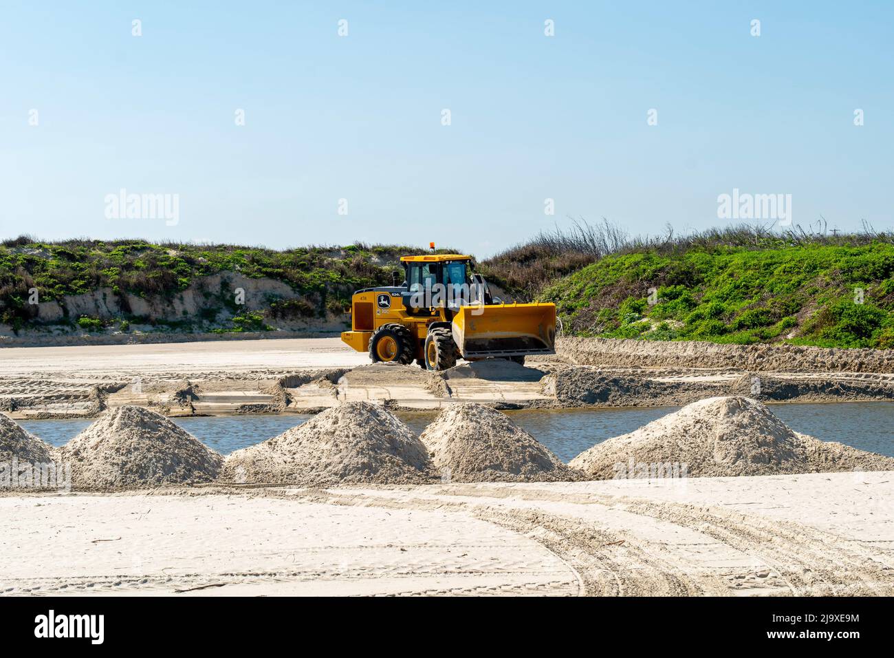 PORT ARANSAS, TX - 20200213: Il caricatore frontale Caterpillar livella i cumuli di sabbia intorno a un laghetto, come parte di un progetto di riparazione dopo l'uragano Harvey al Foto Stock