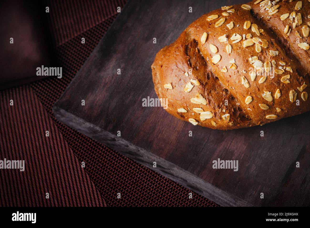 Da vicino a un rustico pane di avena, fatto in casa su un asse di legno, pane multigrain Foto Stock