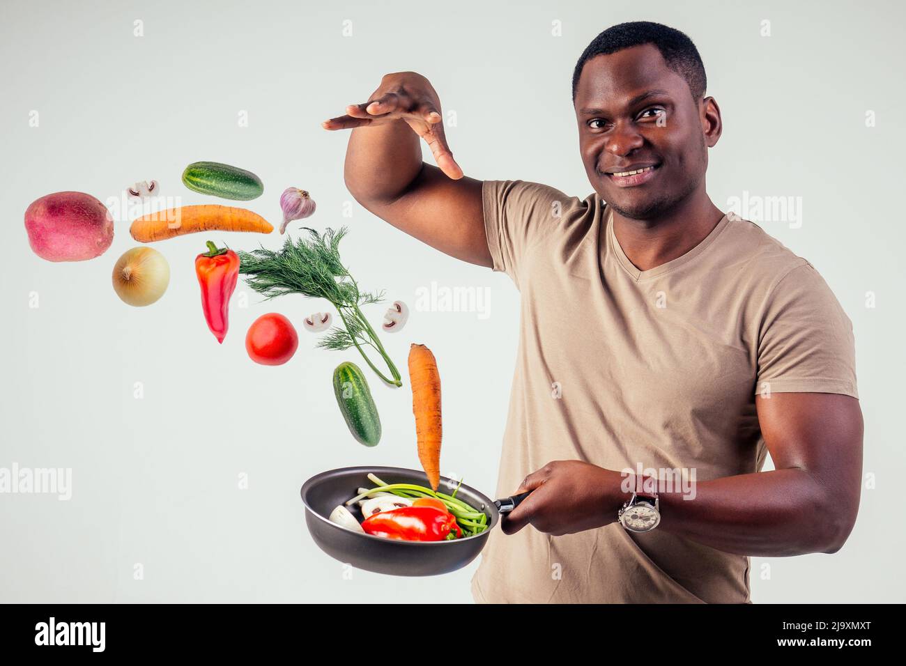 chef afroamericano kitchener che tiene una padella wizard man cucina magica flying food insalata, carota, aglio, cipolla, pepe, patate, cetrioli Foto Stock