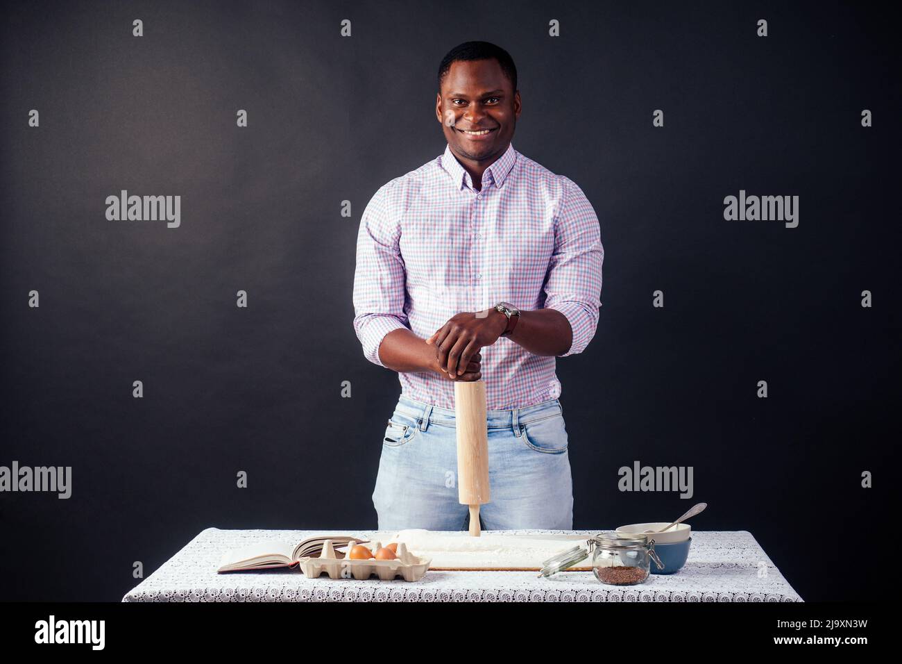 Bello e giovane afro africano uomo che prepara torte fatte in casa American Pie da pasta fresca mani sporche di farina, sul tavolo sono le uova, rolling pin Foto Stock