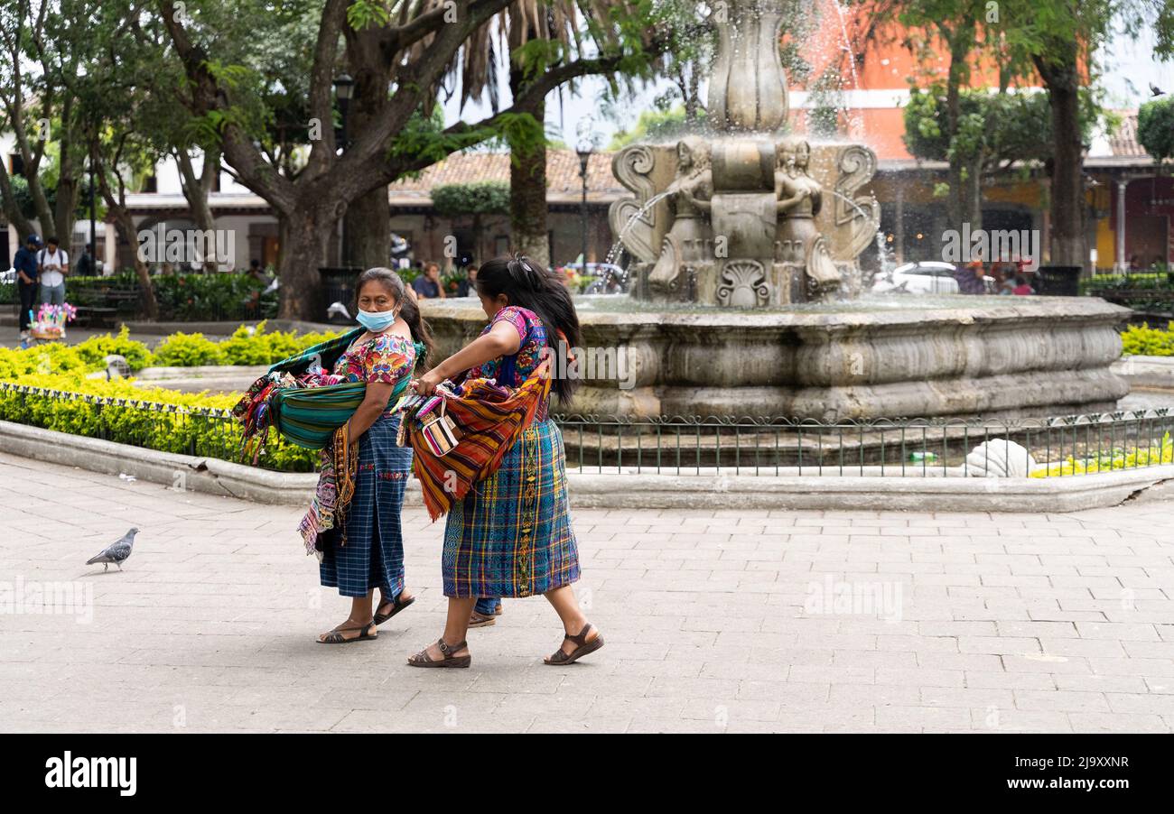 Due donne indigene Maya che vendono merci camminano su Plaza Central Park ad Antigua Guatemala Foto Stock
