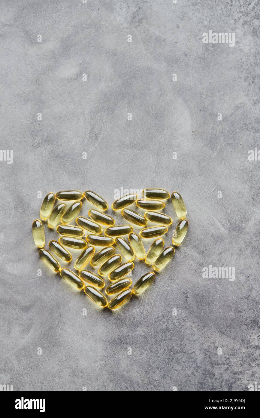 Capsule a forma di cuore omega-3 su sfondo grigio. Il concetto di medicina e di vita sana. Vista dall'alto. Foto Stock