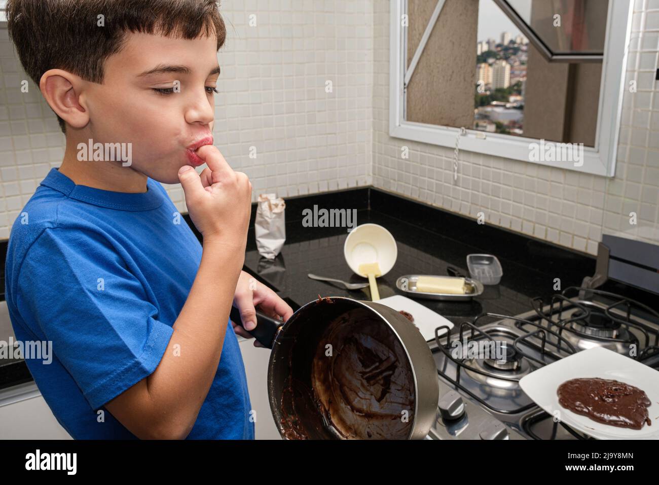 Primo piano di un bambino di 8 anni in cucina tenendo una padella e leccando il dito. Foto Stock