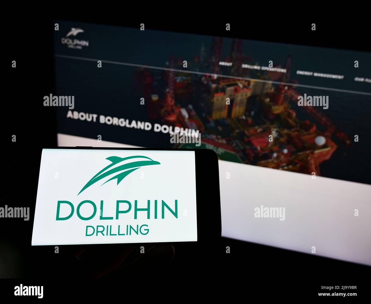 Persona che tiene il cellulare con il logo della società Dolphin Drilling Holdings Limited sullo schermo di fronte al sito web aziendale. Mettere a fuoco sul display del telefono. Foto Stock