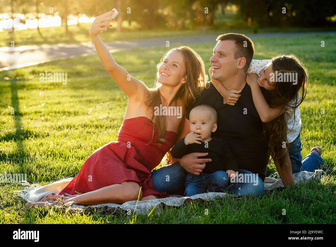 felice famiglia bella madre (donna), bel padre (uomo) con una bambina figlia (scolgirl) e bambino ragazzo figlio fotografato selfie al telefono Foto Stock