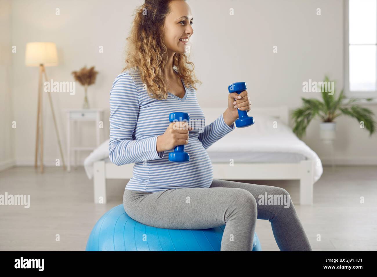Bella e attiva giovane donna incinta con manubri e fit ball facendo sport allenamento a casa Foto Stock