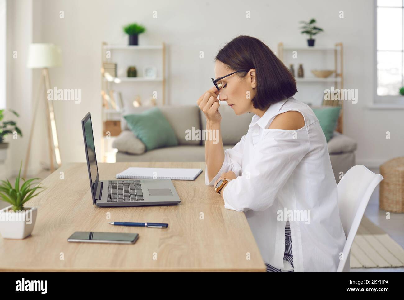 Donna stressata e stressata, seduta alla scrivania con computer portatile Foto Stock
