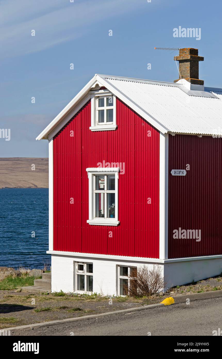 Hvammstangi, Islanda, 1 maggio 2022: Piccola casa a tre piani con soffitta e seminterrato e facciata rossa in metallo ondulato con vista sul fiordo Foto Stock