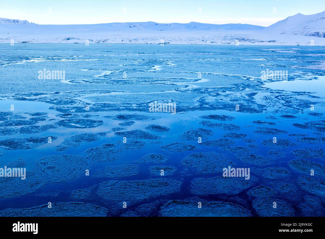 Un'ora blu d'inverno vista mattutina attraverso la laguna di Jökulsarlön iceberg senza ghiaccioli presenti. La laguna è coperta da uno strato rotto di ghiaccio sottile. Foto Stock