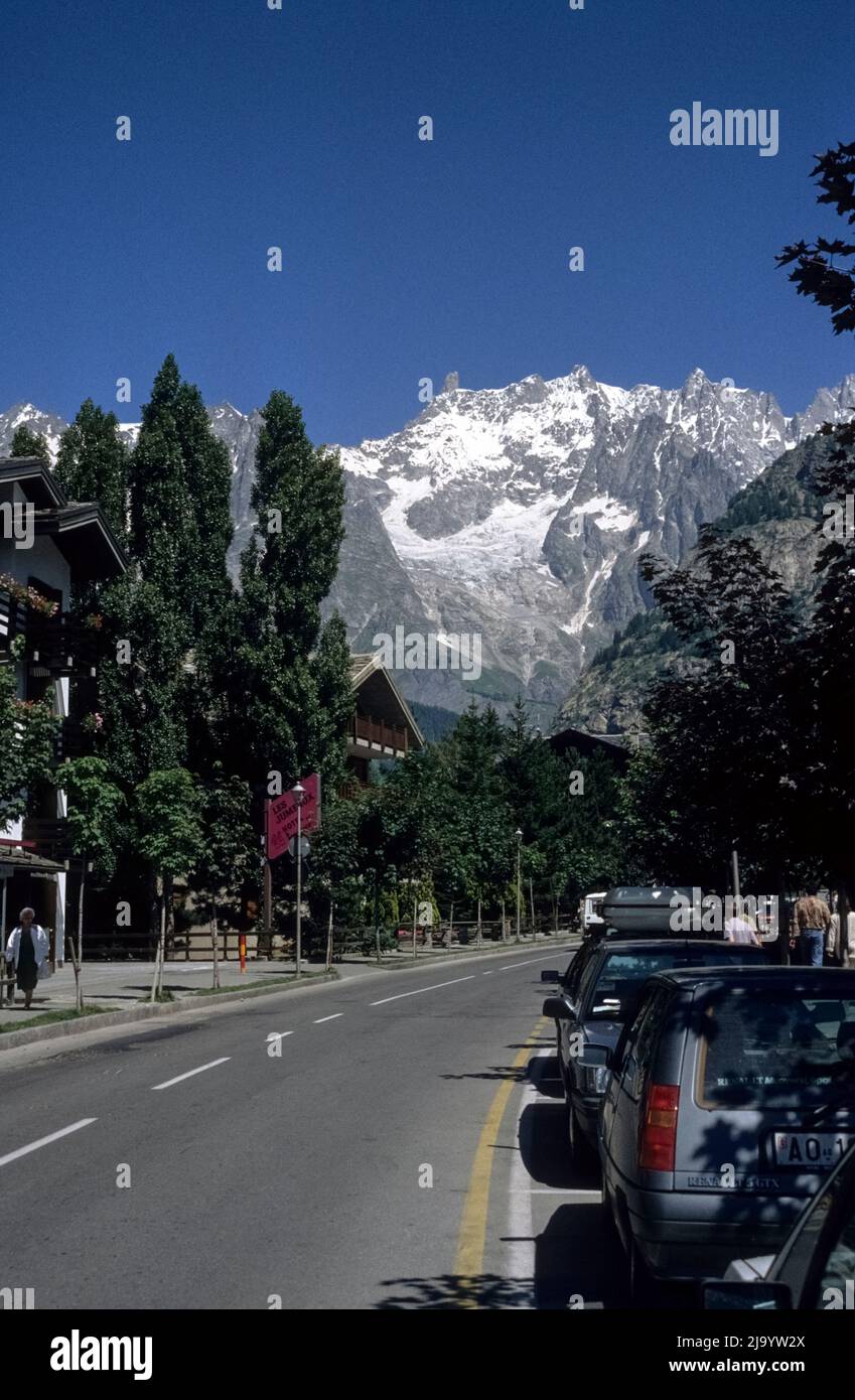 Le auto sono parcheggiate in Via Regionale. Sullo sfondo il massiccio del Monte Bianco con il ghiacciaio della Brenva. Courmayeur, Valle d'Aosta, Italia, 1990 Foto Stock