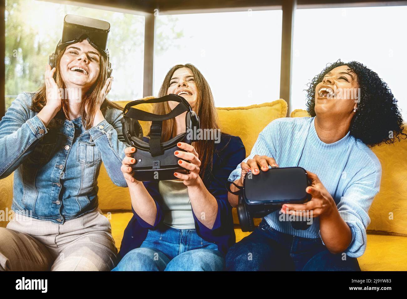 il gruppo interrazziale di giovani donne è divertito dopo un'esperienza di realtà simulata immersiva - le ragazze ridono insieme a 3d cuffie verso il basso - vivido sbiadito Foto Stock