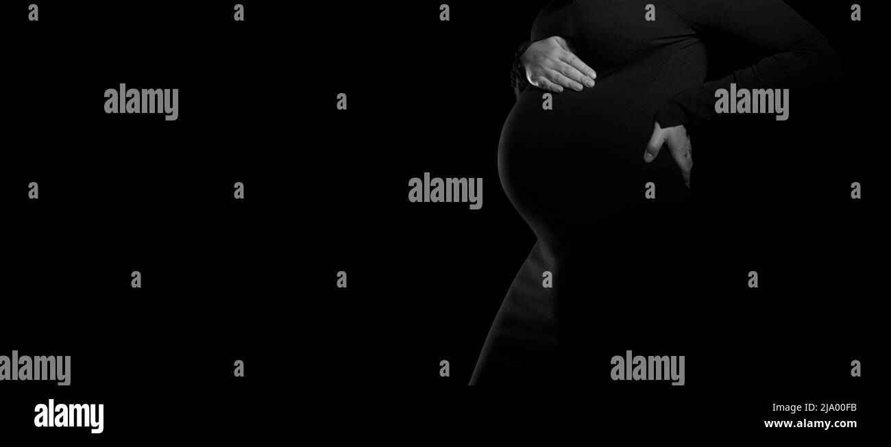 Panorama della vista laterale della donna incinta in abito nero su sfondo nero Foto Stock