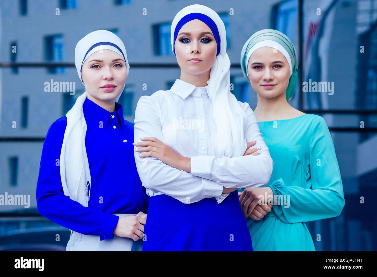 gruppo di tre donne d'affari musulmane donna caucasica in elegante hijab e turban che lavorano sulle finestre di sfondo di ufficio di strada di un grattacielo Foto Stock