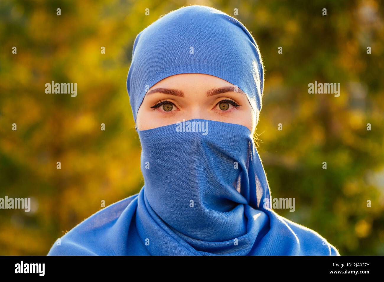 Ritratto di bella donna musulmana con occhi verdi che indossa il volto blu sciarpa chiuso coperto di aveil sfondo alberi di foresta nel parco Foto Stock