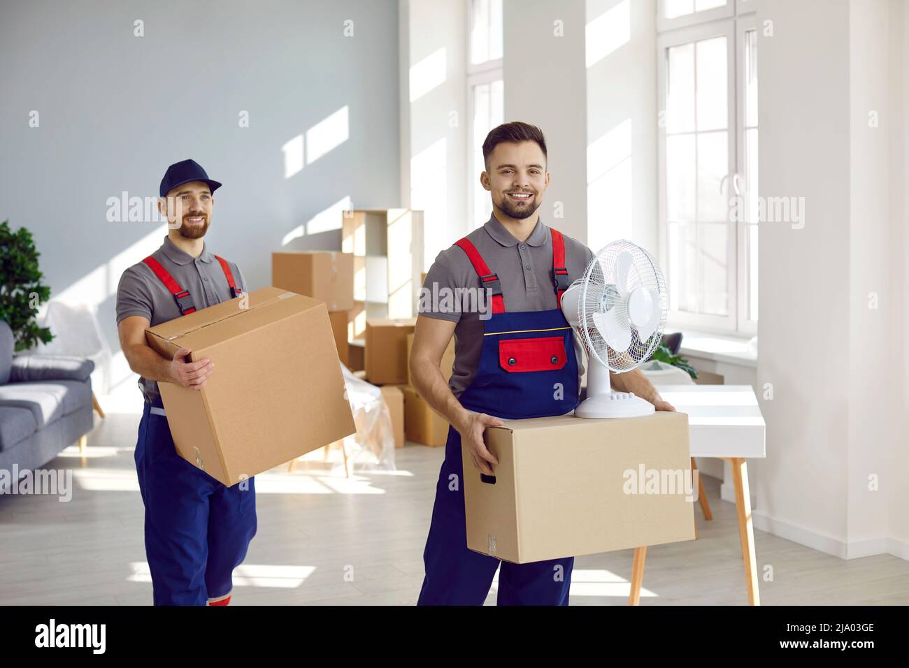 Due addetti ai servizi di consegna e movimentazione felici che trasportano scatole di cartone e altro materiale Foto Stock