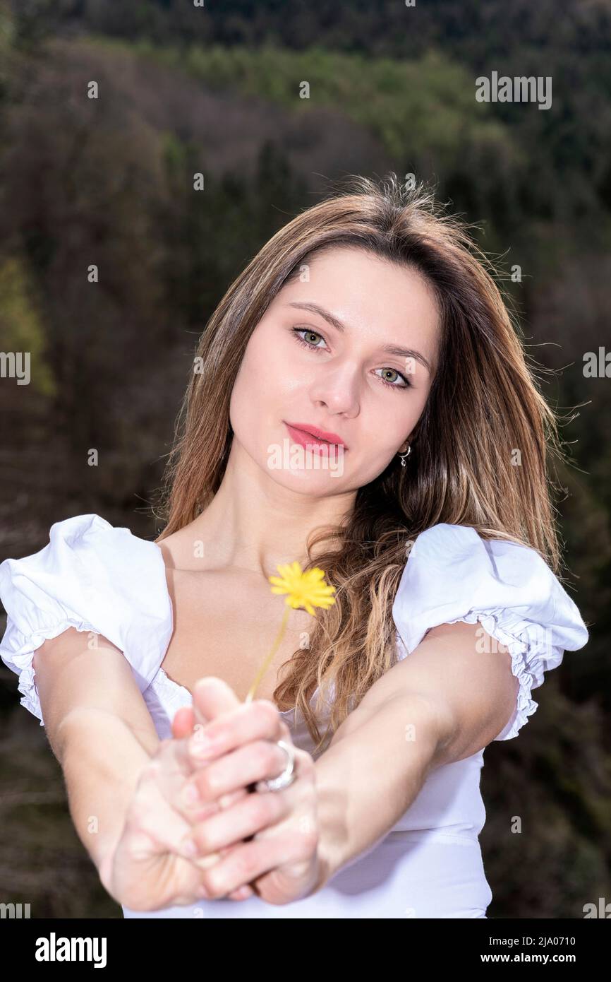 donna bionda vestita di bianco offrendo un fiore alla macchina fotografica Foto Stock
