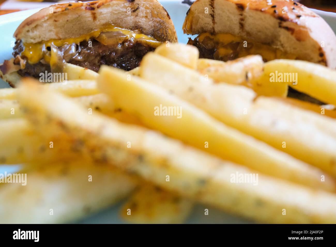 Primo piano con delizioso hamburger con formaggio, patate fritte e cipolla caramellata in un piatto. Fuoco selettivo di carne e pane. Foto Stock