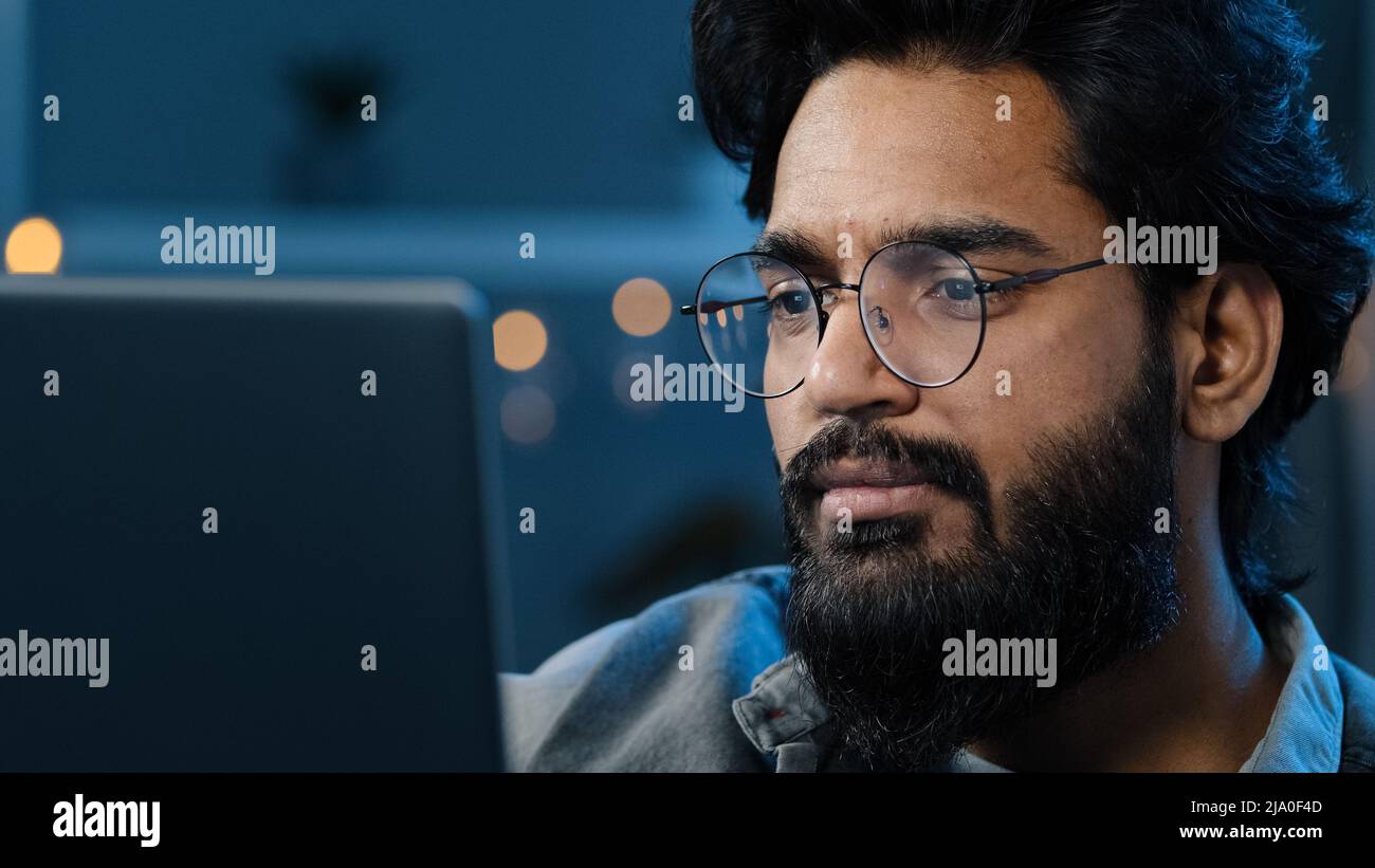 Pensieroso indiano arabo bearded uomo adulto che pensa alla soluzione di problema che lavora sul laptop a casa dubbioso volto maschio in occhiali guardando il computer Foto Stock