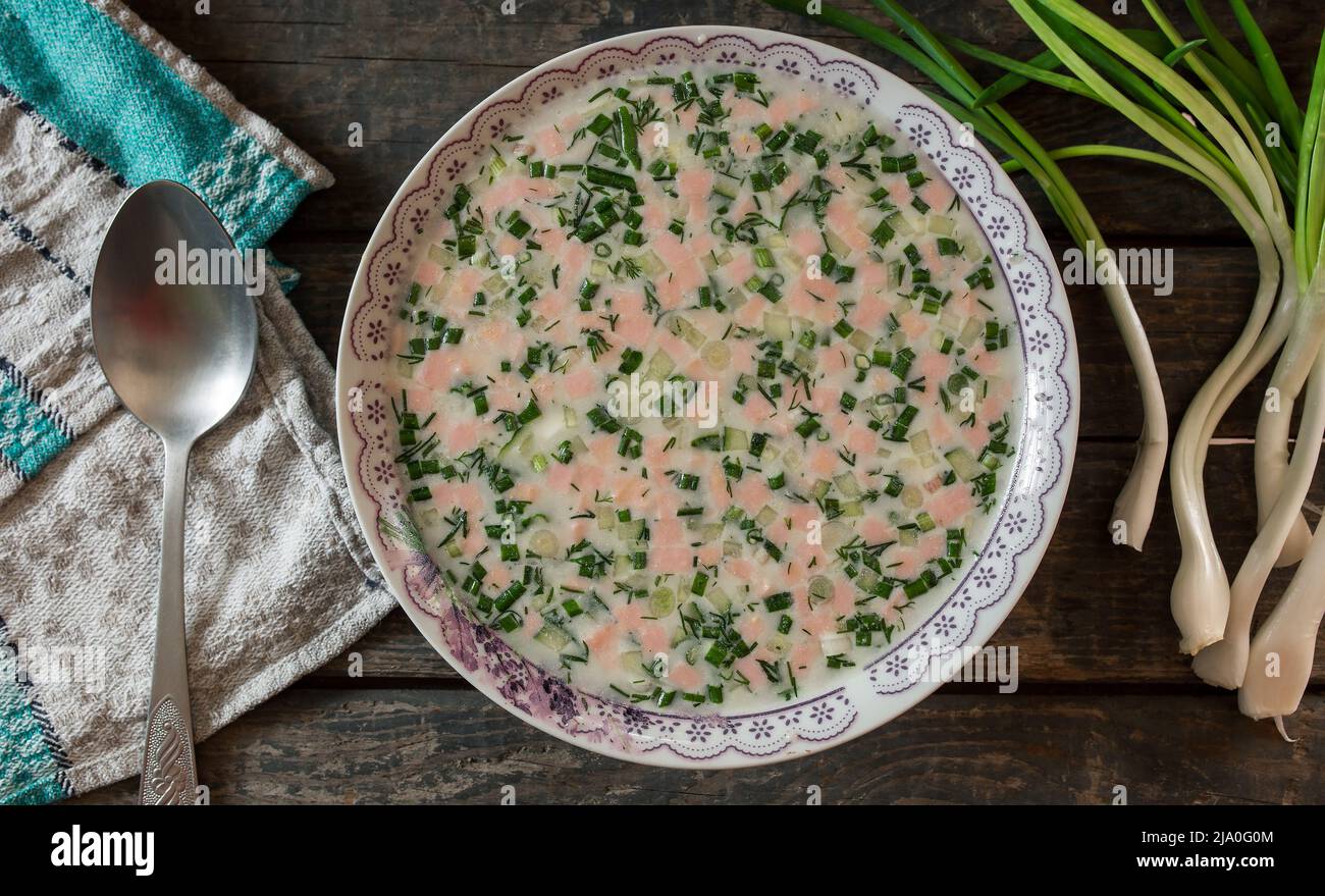 Piatto di okroshka su un tavolo di legno. Cucchiaio su asciugamano e cipolla verde Foto Stock