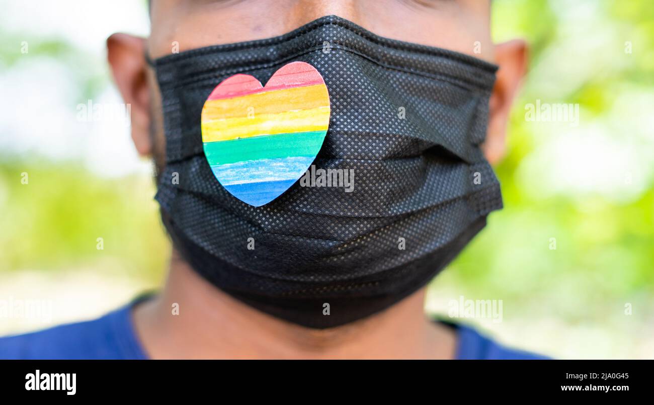 primo piano colpo di uomo con orgoglio o simbolo di cuore arcobaleno sulla maschera medica del viso durante coronavirus covid-19 pandemic pride march - concetto di solidarietà Foto Stock