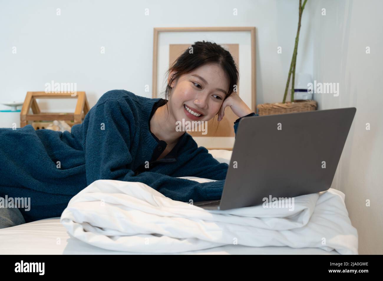 Bella ragazza asiatica godendo un film sul suo portatile. Ragazza adolescente cute che guarda i video in linea a letto Foto Stock