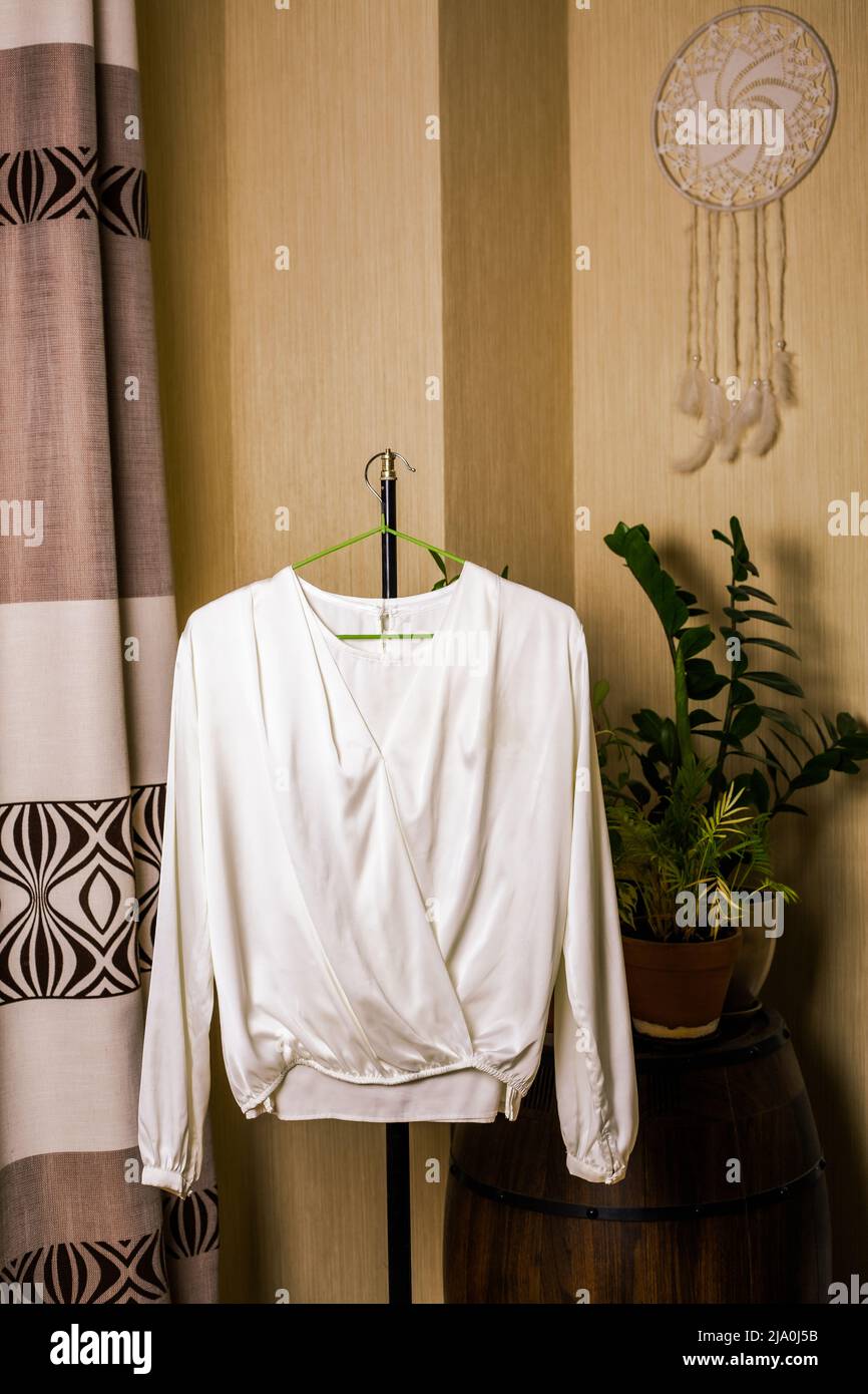 Blusa di seta bianca fatta a mano appesa ad un appendiabiti in camera. Foto Stock