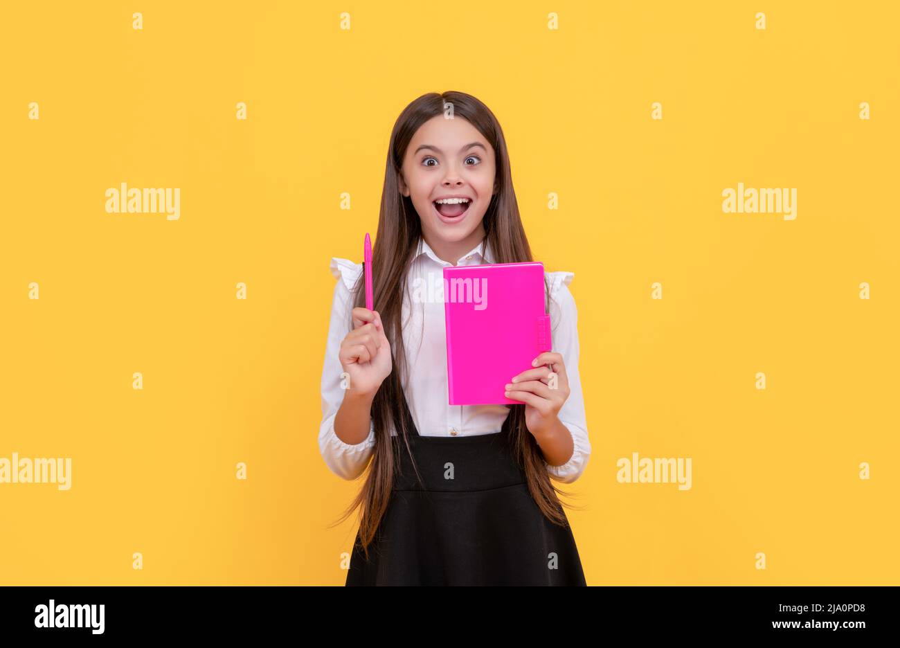 Felice bambino genio tenere libro scuola puntando penna su sfondo giallo, idea Foto Stock