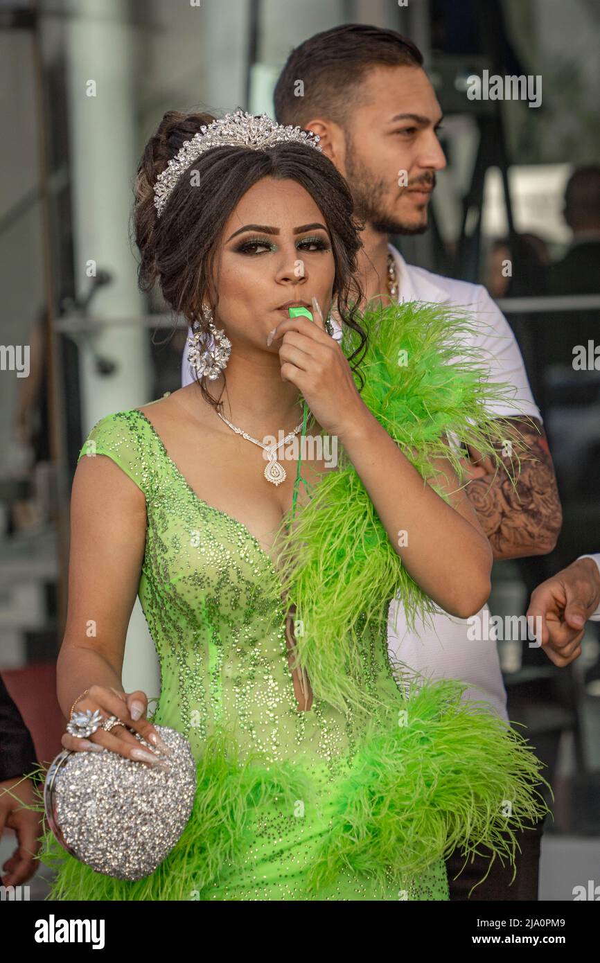 Sofia, Bulgaria - 24.05.2022, Una ragazza gessata in un abito verde fantasia soffia un fischio al Prom Graduate Foto Stock