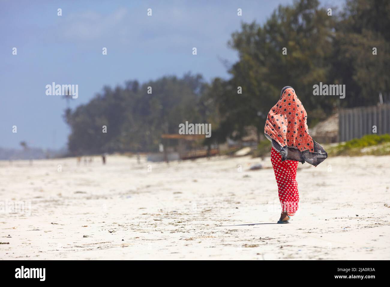 Una donna in abiti musulmani tradizionali cammina sulla spiaggia di Zanzibar, Tanzania, Africa. Foto Stock