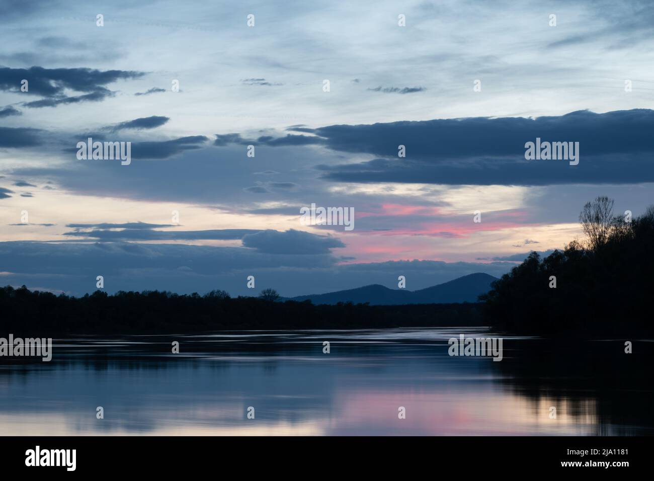 Paesaggio di fiume e silhouette di montagna al crepuscolo, fiume Sava con riva boscosa e montagna Motajica con le nuvole nel cielo durante l'ora blu e porpora Foto Stock
