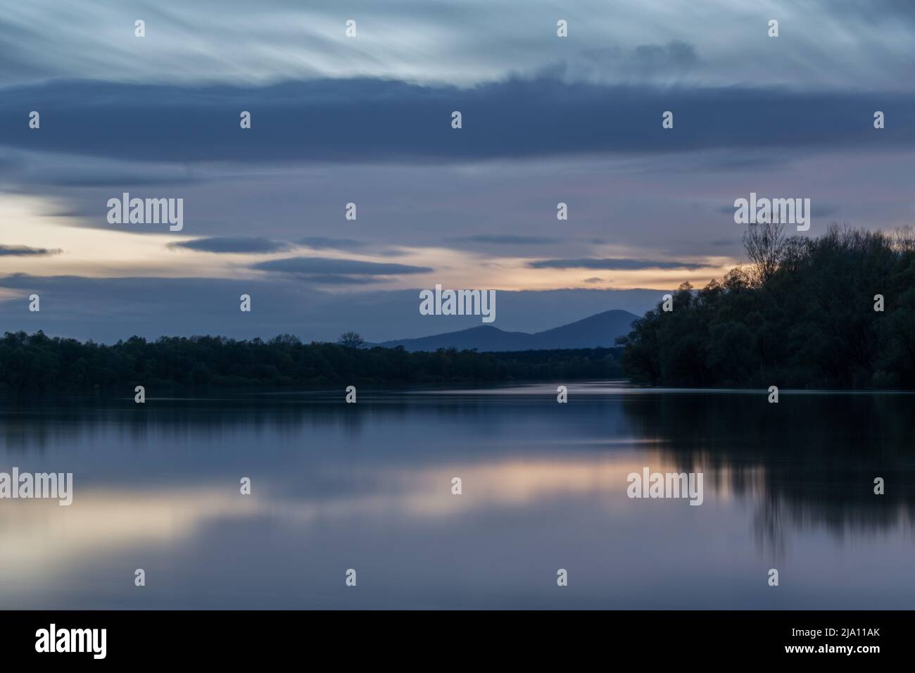Paesaggio di fiume e silhouette di montagna al crepuscolo, fiume Sava con riva boscosa e scena montana Motajica con nuvole nel cielo durante l'ora blu Foto Stock