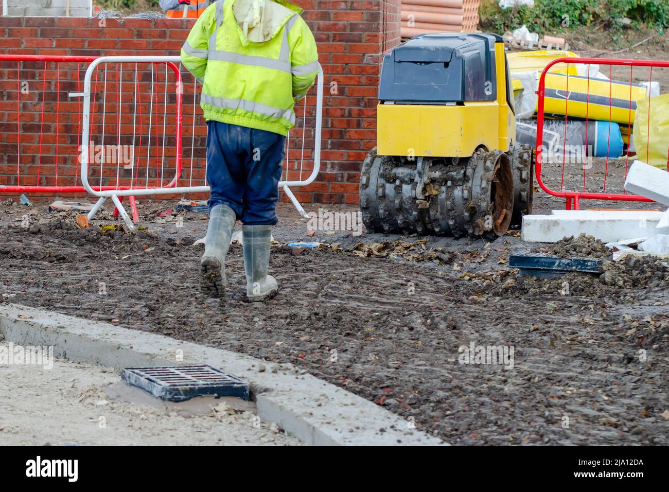 Lavoratori edili che operano un compattatore per trincee controllato a distanza per compattare il terreno intorno a una nuova casa residenziale Foto Stock
